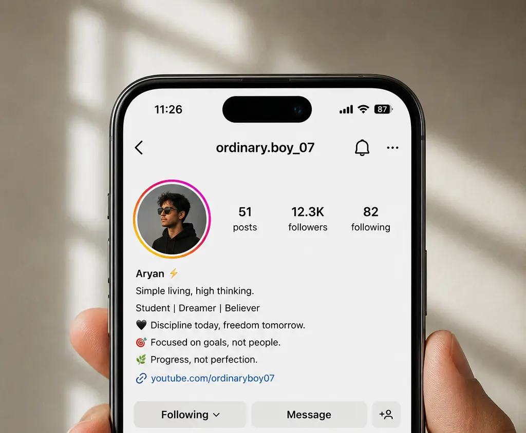 Realistic close-up of a hand holding a smartphone displaying an Instagram profile for a young man. The profile features a clean and simple bio, profile picture, follower statistics, story highlights, and a lifestyle-themed photo grid. Soft natural lighting and a neutral background create a modern, aesthetic look that emphasizes a minimalist Instagram profile design for boys.