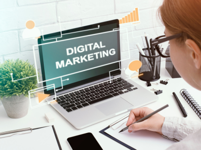 Digital marketing workspace showing a person working on a laptop displaying “Digital Marketing,” with a notebook, pen, and office supplies on a desk.